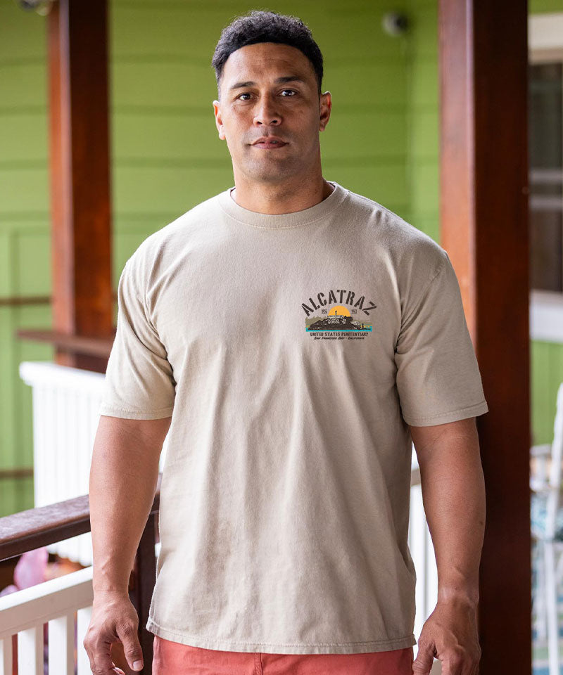 Man wearing a beige t-shirt with 'Alcatraz' logo on a wooden porch. View 3
