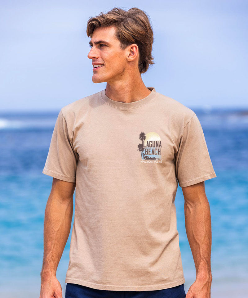 Man wearing a beige t-shirt with a 'Laguna Beach' logo on a beach View 3