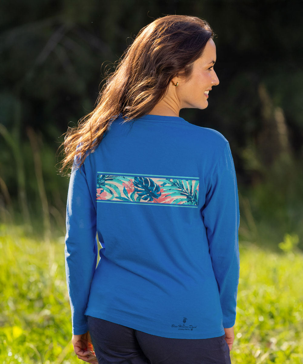 A woman wearing a bright blue long-sleeve shirt with a tropical leaf print band across the upper back, photographed outdoors in a grassy area. View 3
