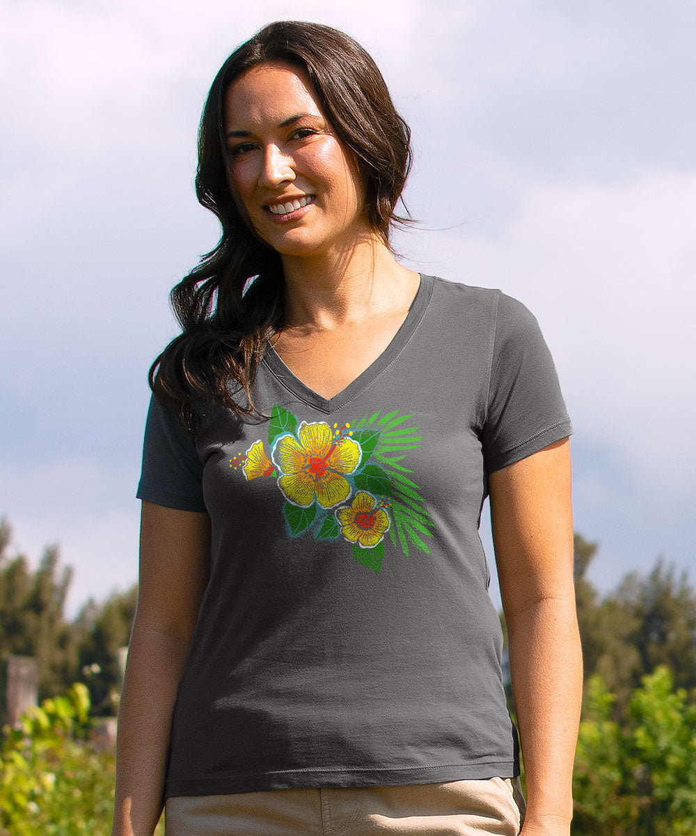 A woman wearing a dark gray v-neck t-shirt with a colorful graphic of yellow hibiscus flowers and green leaves, set against an outdoor background of sky and trees. View 2