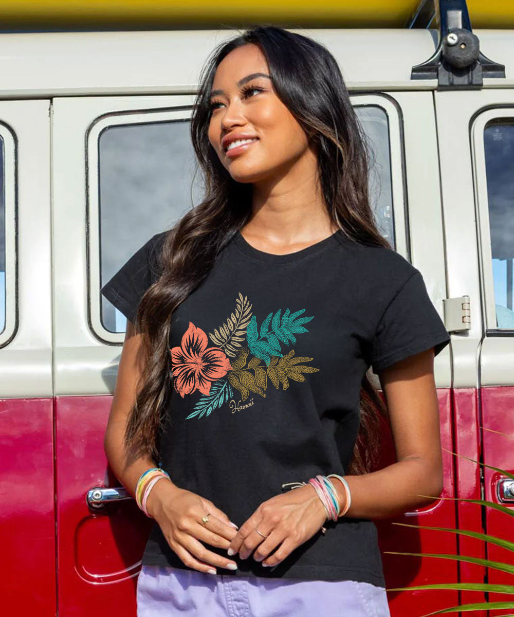 A woman wearing a black short-sleeve t-shirt with a colorful tropical floral and leaf graphic, standing in front of a vintage red and white van. View 2
