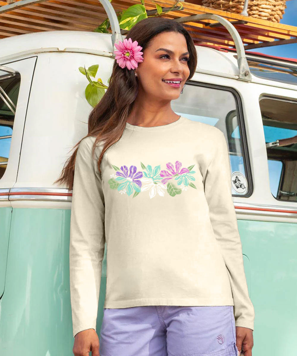 A woman wearing a cream-colored long-sleeve t-shirt with a colorful floral graphic on the chest, standing in front of a retro-style mint green and white van. View 2