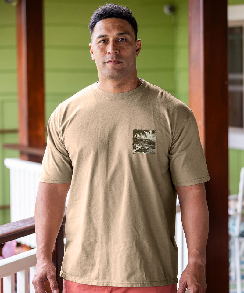Man wearing a beige t-shirt with a small graphic on a beach View 3