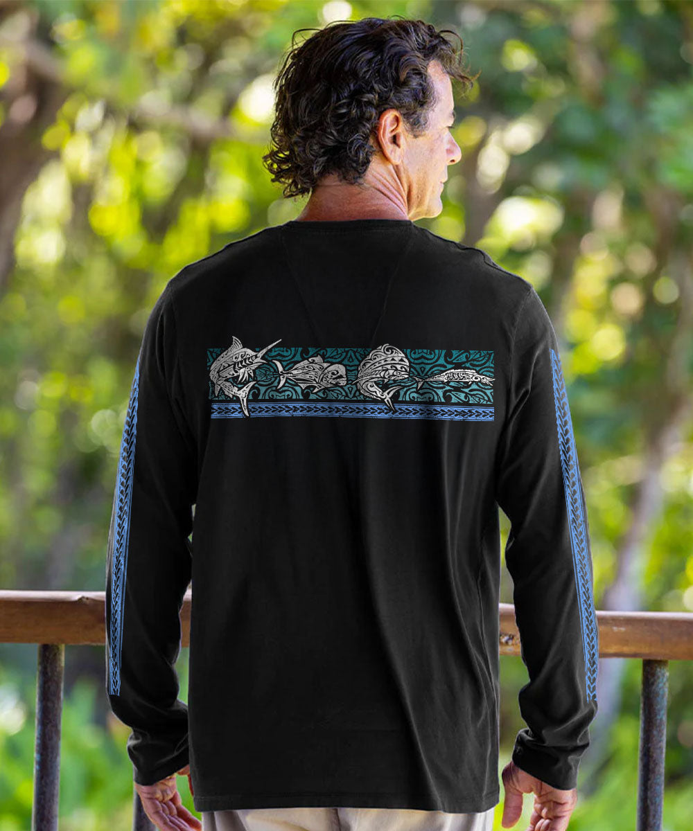 A man viewed from behind wearing a black long-sleeve shirt with a horizontal graphic across the upper back showing fish in white and teal, and teal sleeve stripes, set against a blurred green outdoor background. View 3