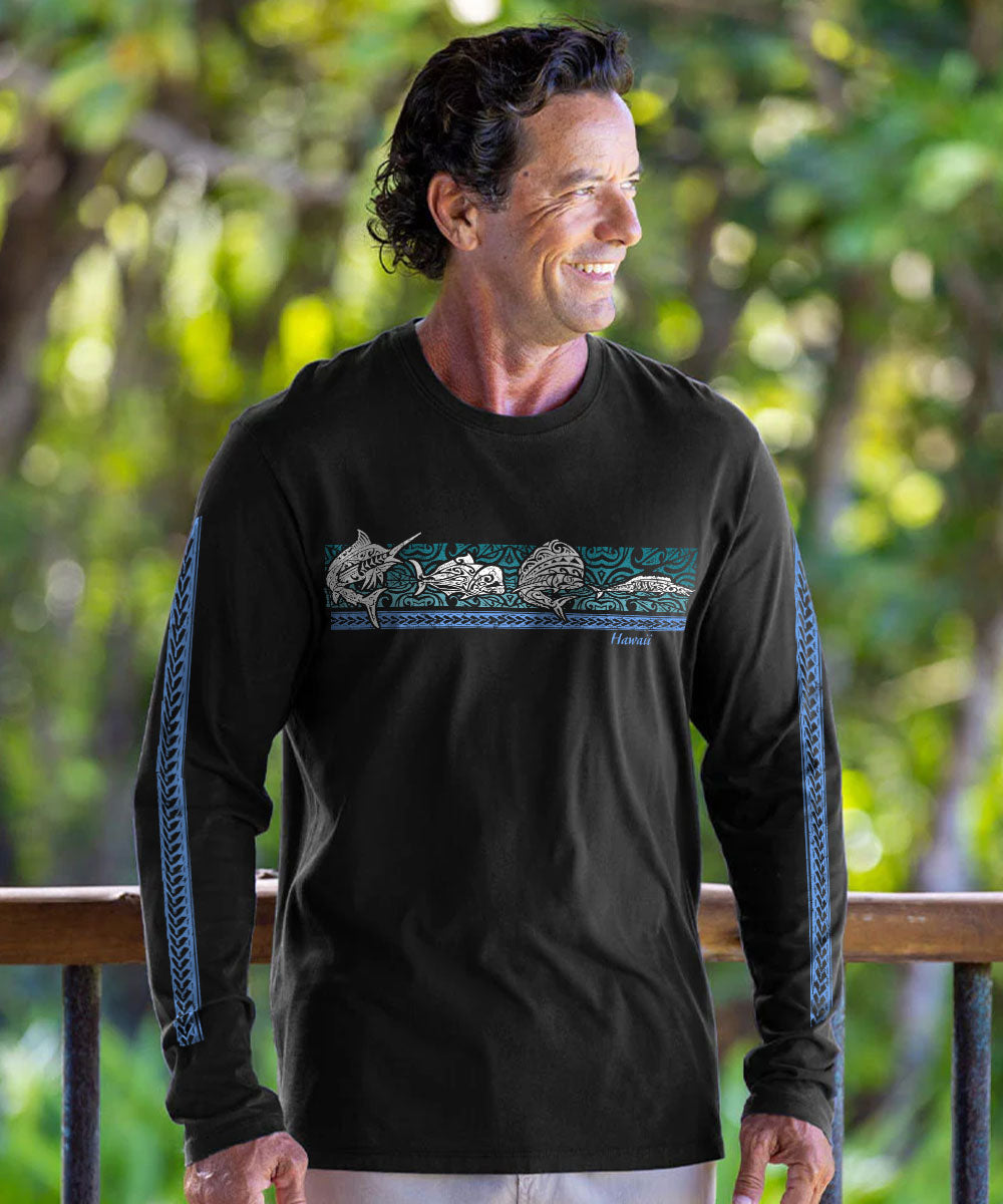 A man wearing a black long-sleeve t-shirt with a horizontal graphic of dolphins and fish in teal, blue, and white, standing outdoors in front of a wooden railing and green foliage. View 2