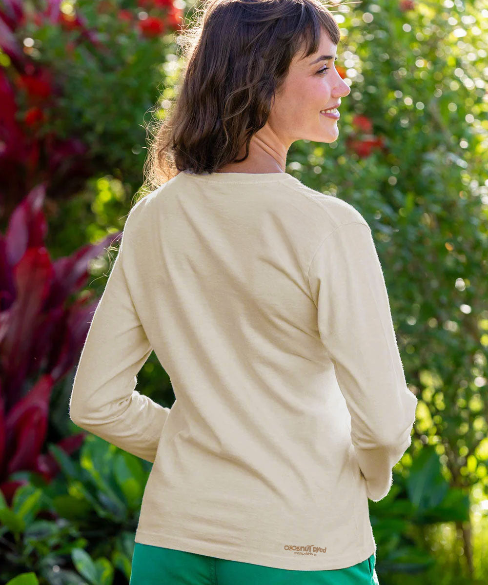 A woman wearing a light beige long-sleeve crewneck shirt, shown from the back in an outdoor garden setting with green foliage and red flowers. View 3