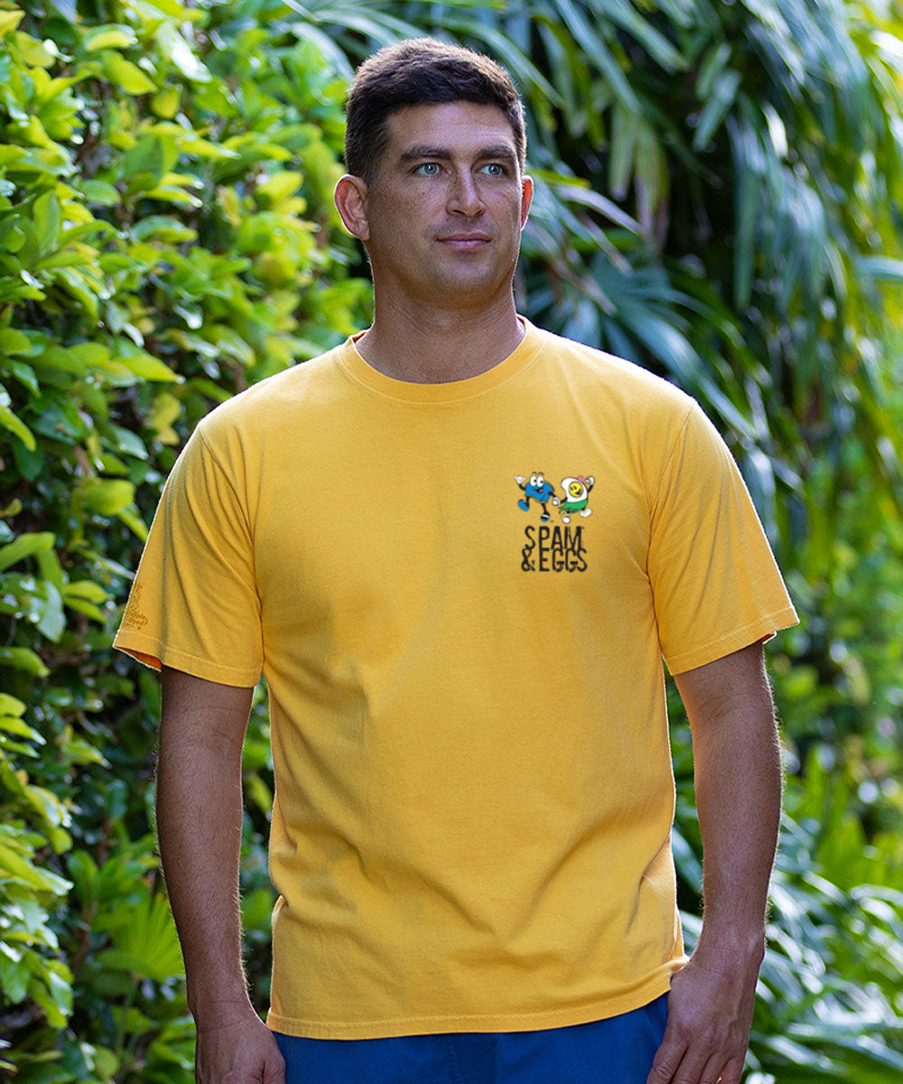 Man wearing a yellow t-shirt with cartoon characters in front of green foliage View 3