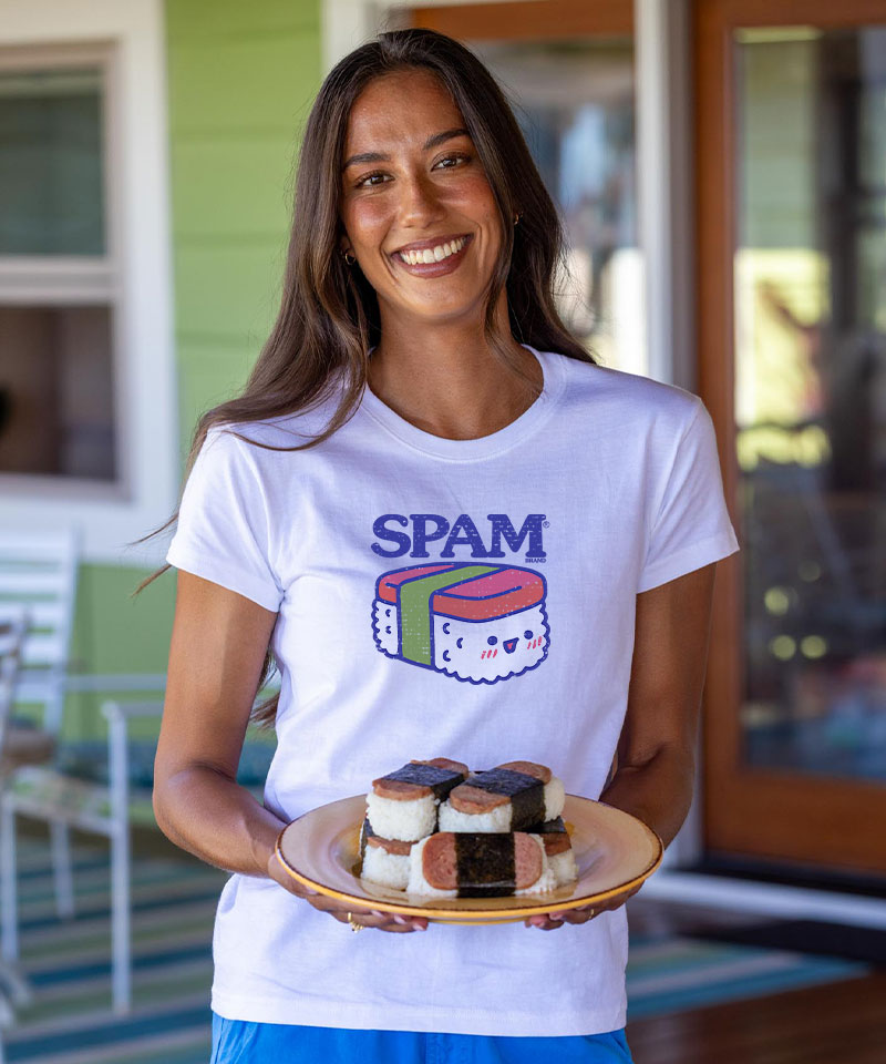 Woman wearing a white t-shirt with 'SPAM' and sushi design, holding a plate of small desserts. View 3