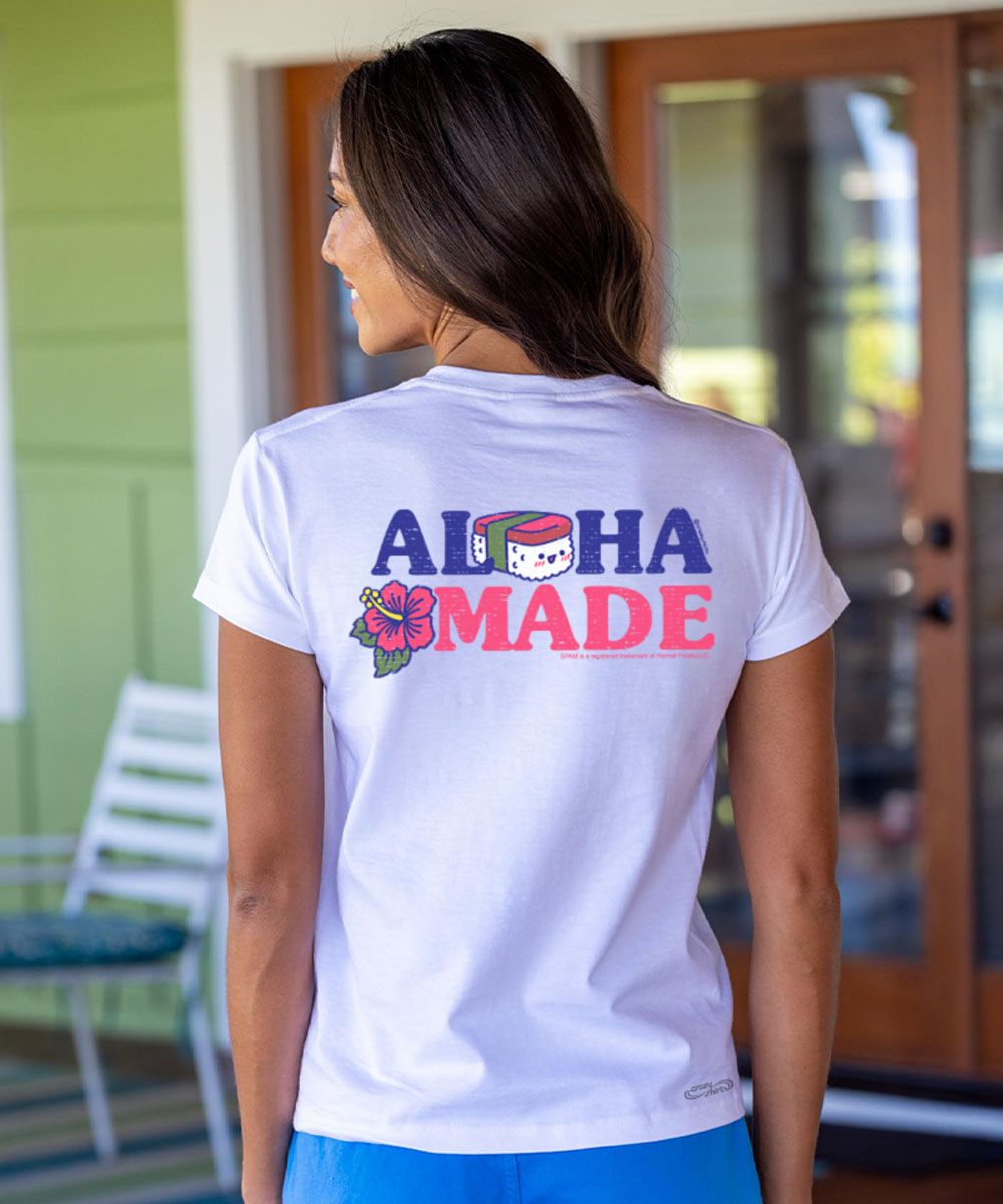 Woman wearing a white t-shirt with 'Aloha Made' text on the back, standing in front of a glass door. View 2