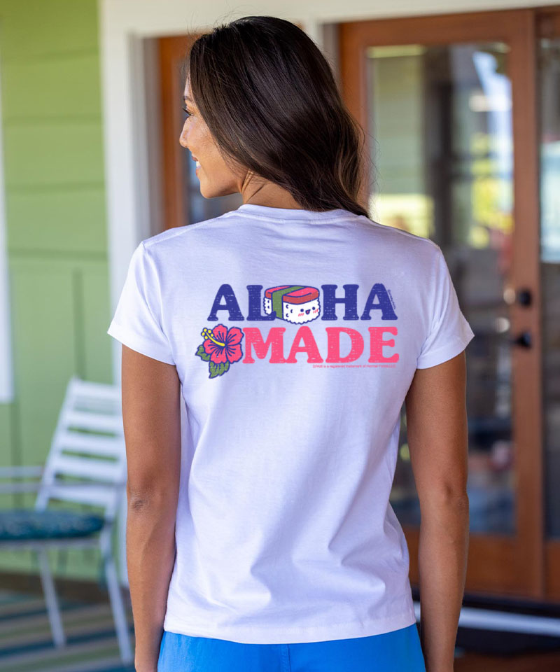 Woman wearing a white t-shirt with 'Aloha Made' text on the back, standing in front of a glass door. View 2