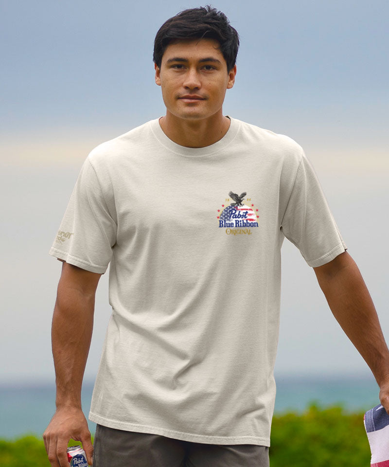 Man wearing a white t-shirt with a logo, standing outdoors with a blurred background View 3