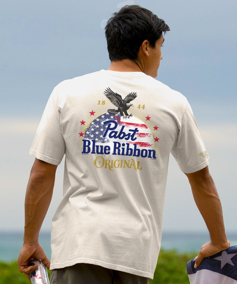 Person wearing a Pabst Blue Ribbon t-shirt with an eagle graphic outdoors. View 2