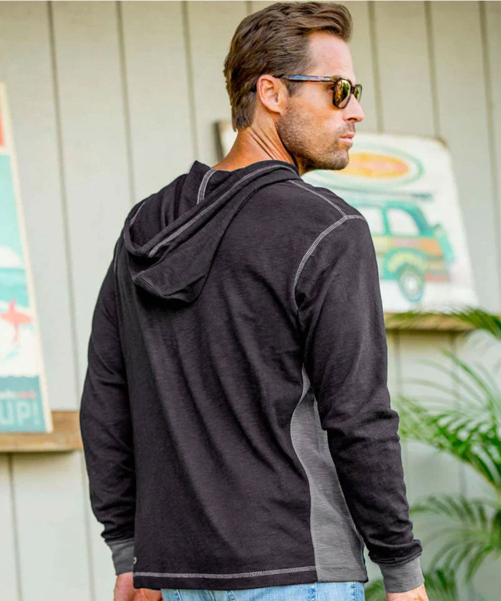 A man wearing a dark charcoal gray hooded long-sleeve shirt with heather gray side panels, shown from the back and side against a light gray wood-paneled wall. View 3