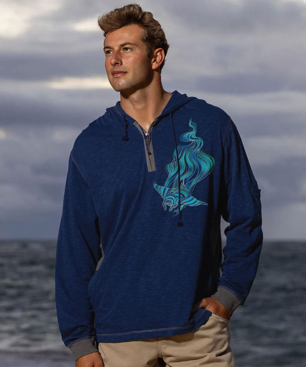 A man wearing a navy quarter-zip long sleeve with a large manta ray on the left chest, standing in front of the ocean.  View 2