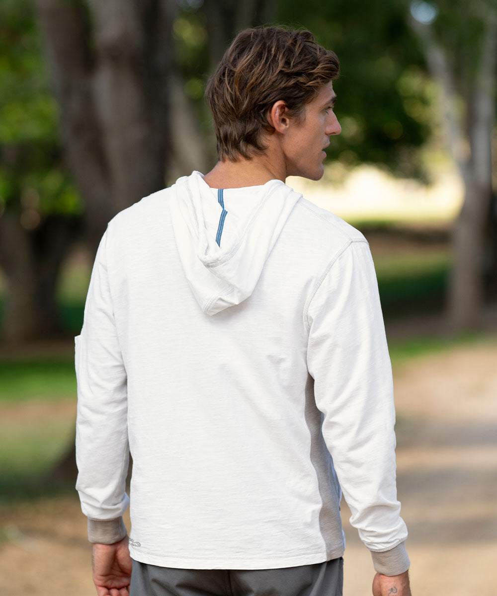 A man wearing a white long-sleeve hooded athletic shirt, shown from the back in an outdoor park setting with blurred trees and a path. View 3