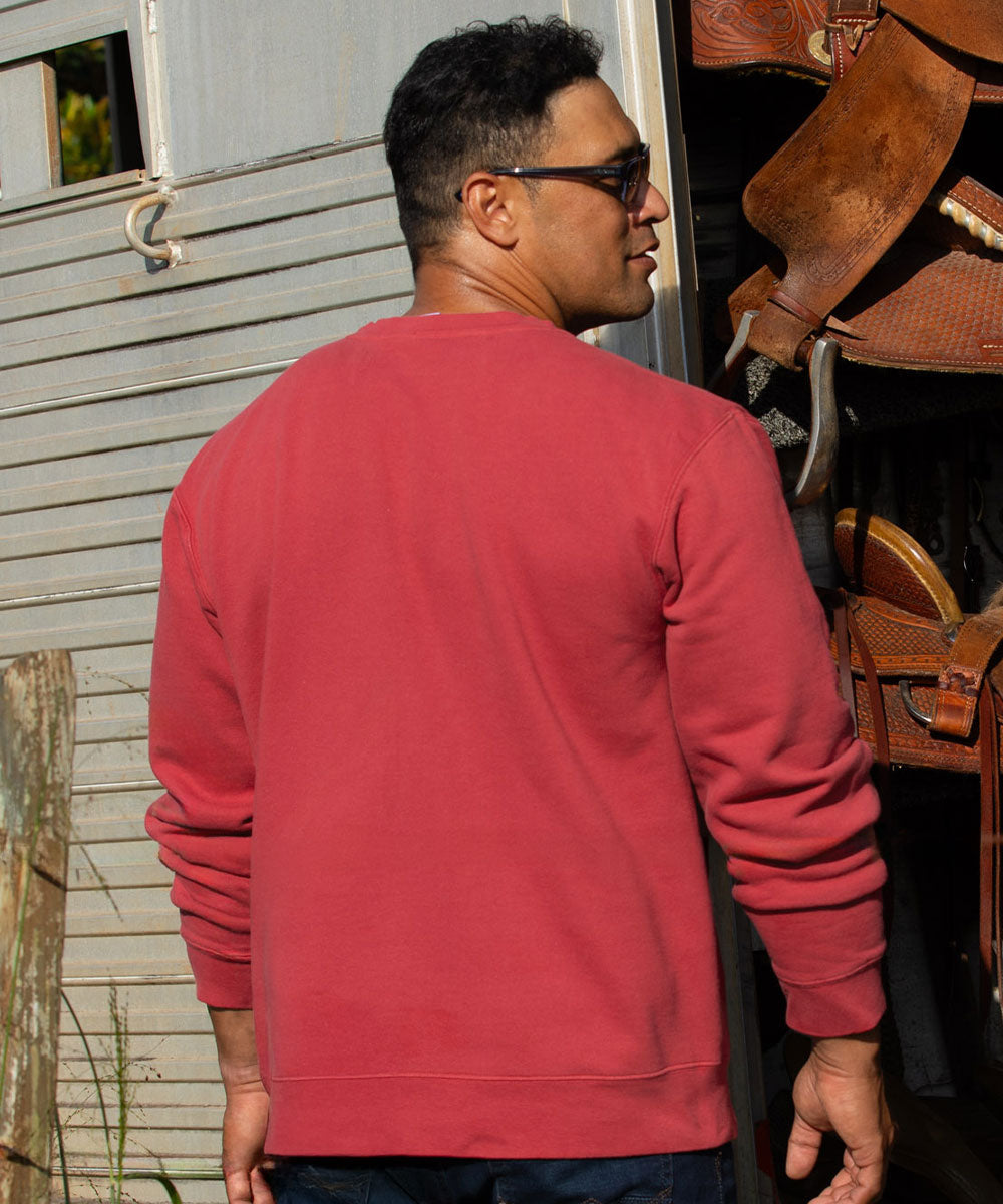 A man wearing a solid red crewneck sweatshirt, viewed from behind, standing in front of a rustic wooden door with leather tack hanging on the right. View 3