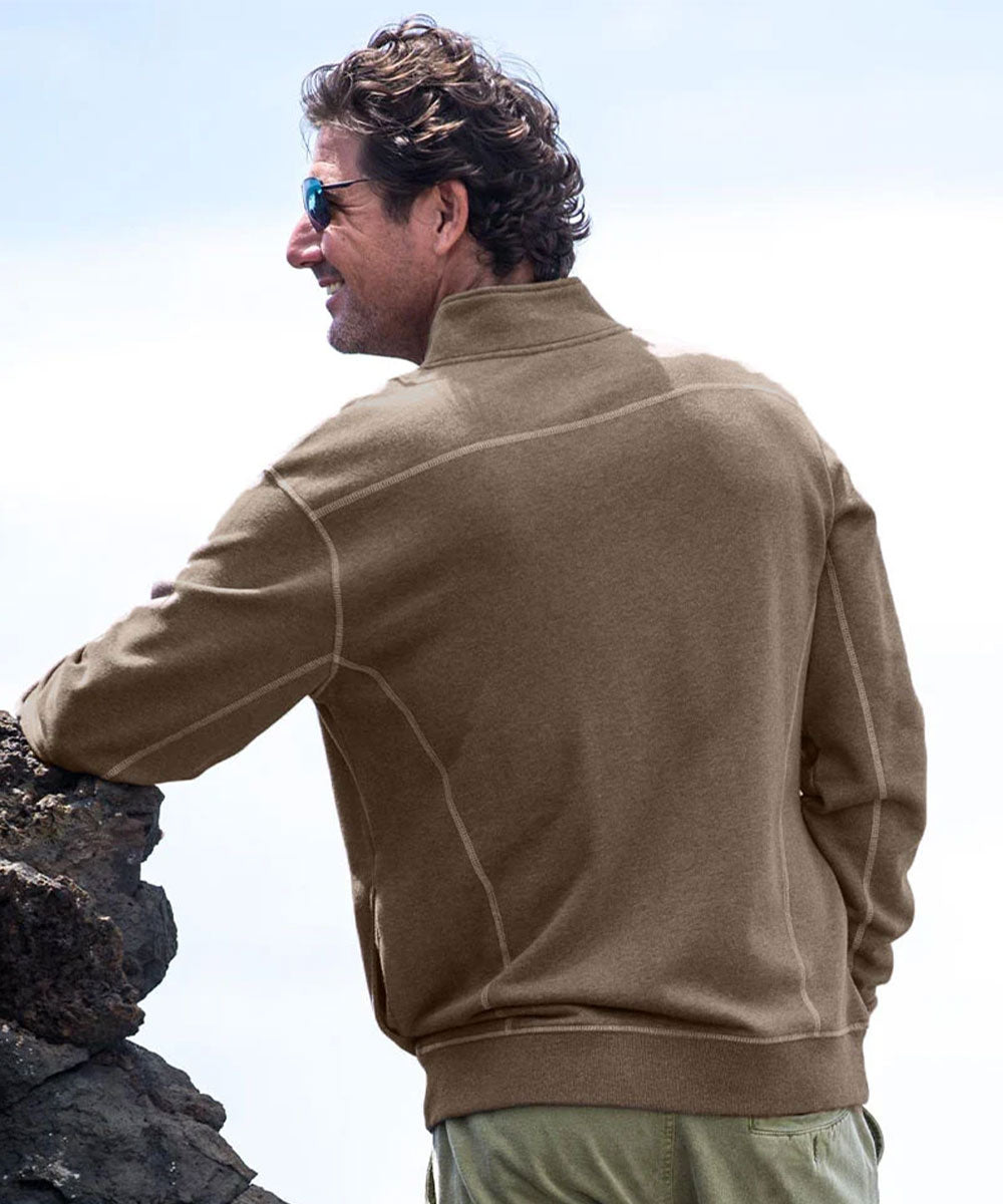 A man wearing a tan quarter-zip fleece pullover outdoors in front of dark volcanic rocks. View 3