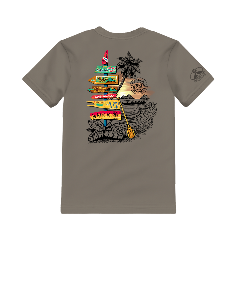 A taupe gray short-sleeve t-shirt shown from the back, featuring a large graphic print of a tropical beach scene with a palm tree, sunset, waves, and colorful directional signs. A small graphic is also printed on the left sleeve. View 1