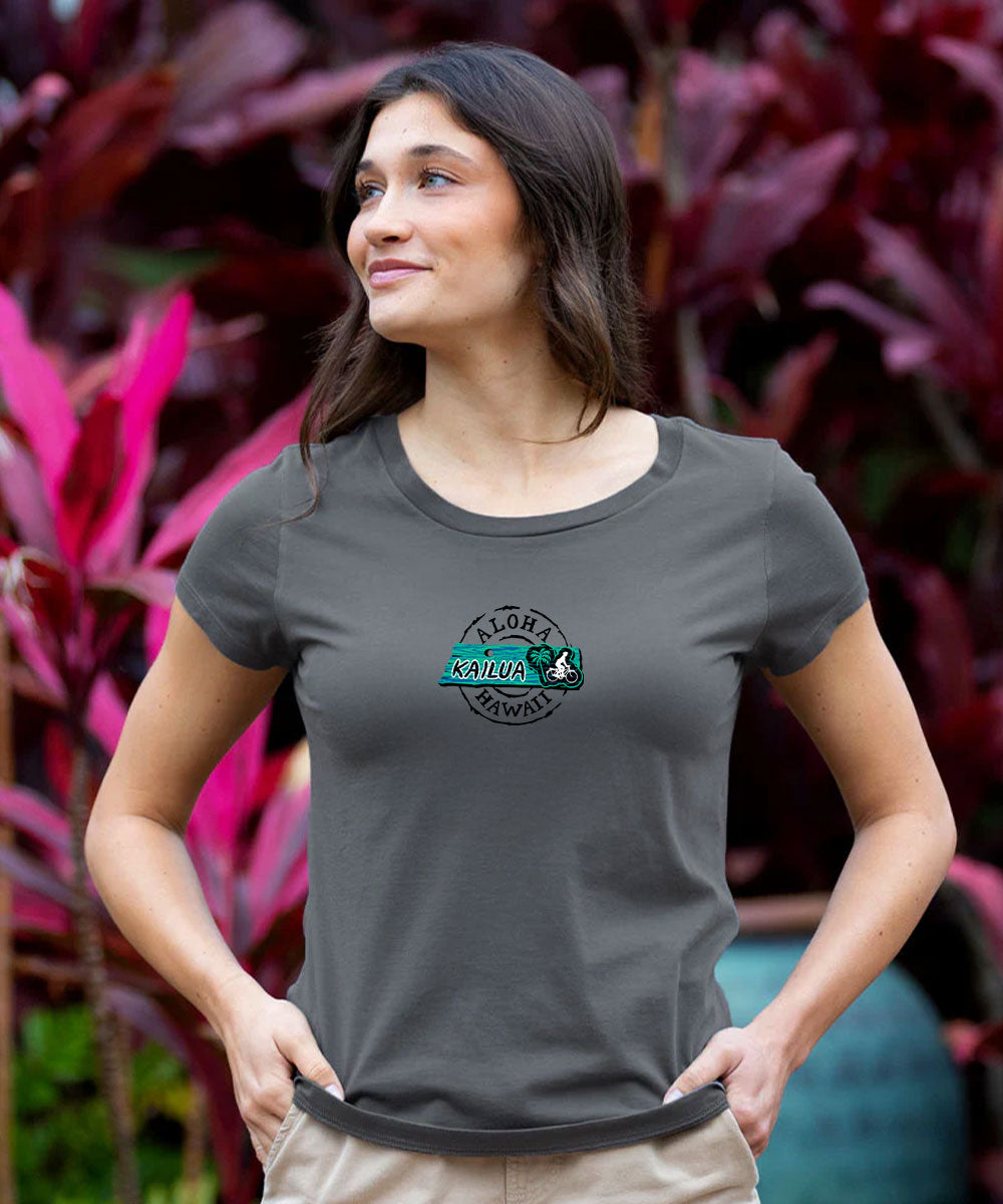 A woman wearing a dark gray t-shirt with a circular 'Albany National' logo on the chest, standing in front of a background of vibrant magenta and green foliage. View 3