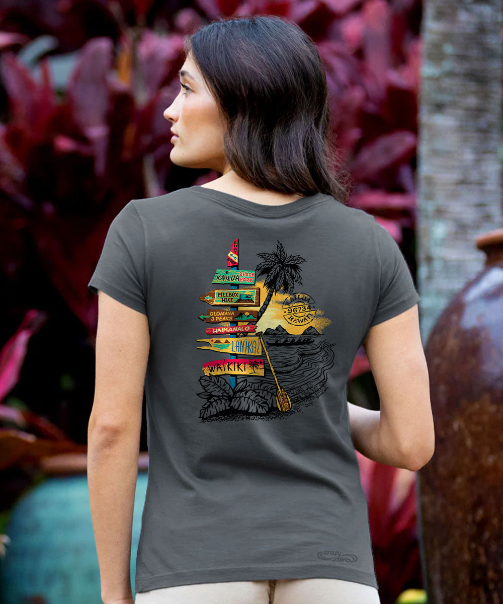 A woman shown from the back wearing a dark gray t-shirt with a colorful graphic print of a tropical island, palm tree, and a signpost reading 'KAWIKO'. View 2