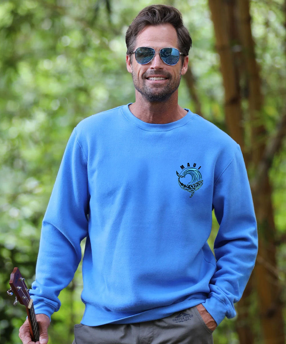 A man wearing a bright blue crewneck sweatshirt with a blue wave graphic on the left chest, standing outdoors in a forest setting. View 3