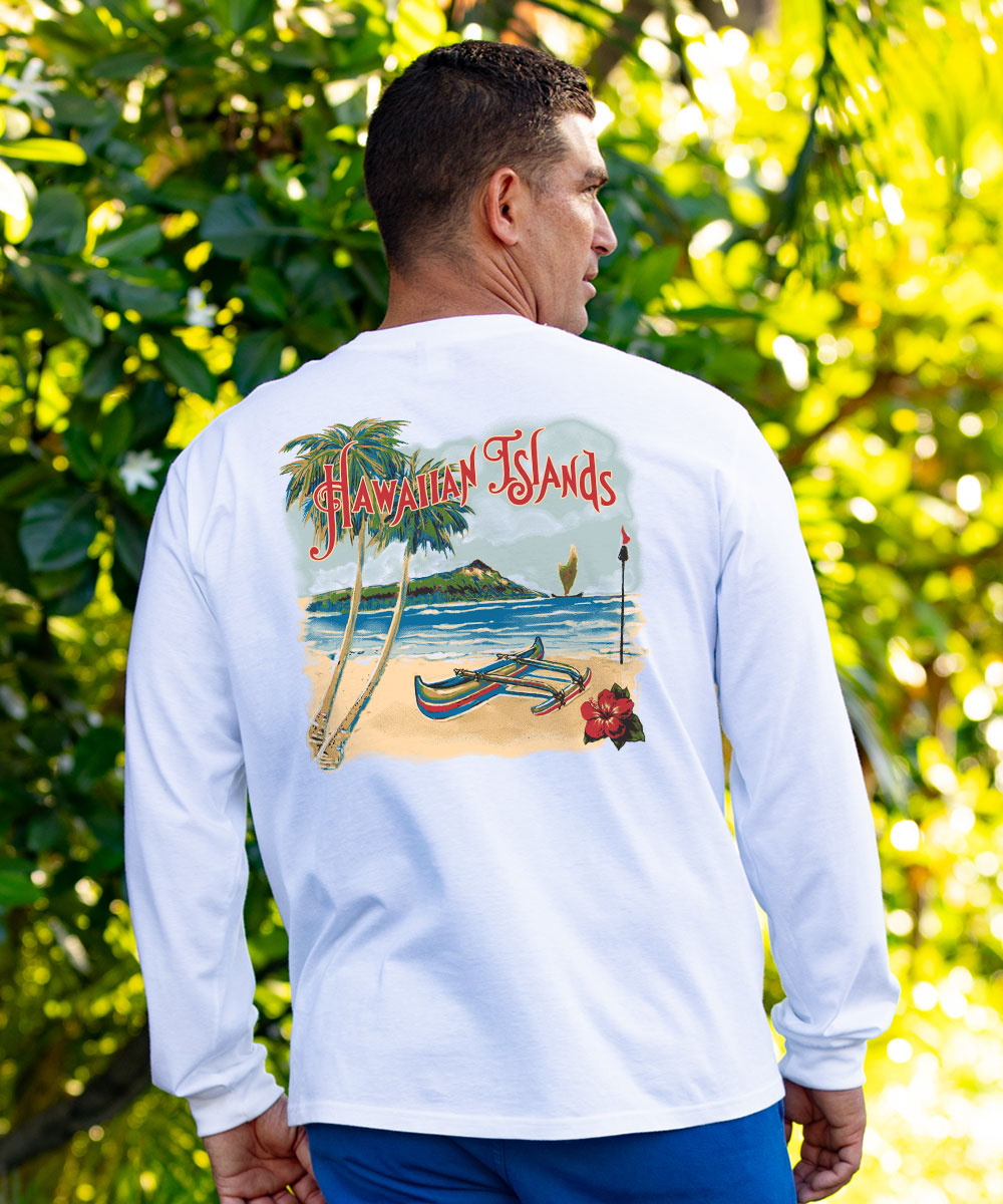 A man viewed from behind wearing a white long-sleeve shirt with a large colorful graphic on the back depicting a tropical Hawaiian Islands beach scene, set against a background of lush green foliage. View 2