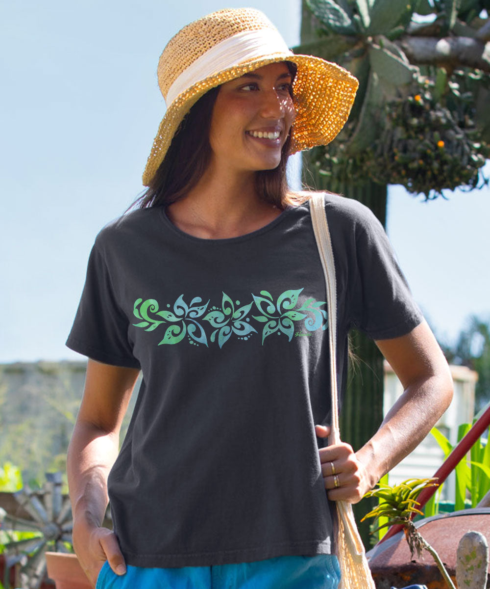 A woman wearing a dark charcoal gray t-shirt with a green and teal floral pattern across the chest, a straw sun hat, and blue pants, standing outdoors. View 2
