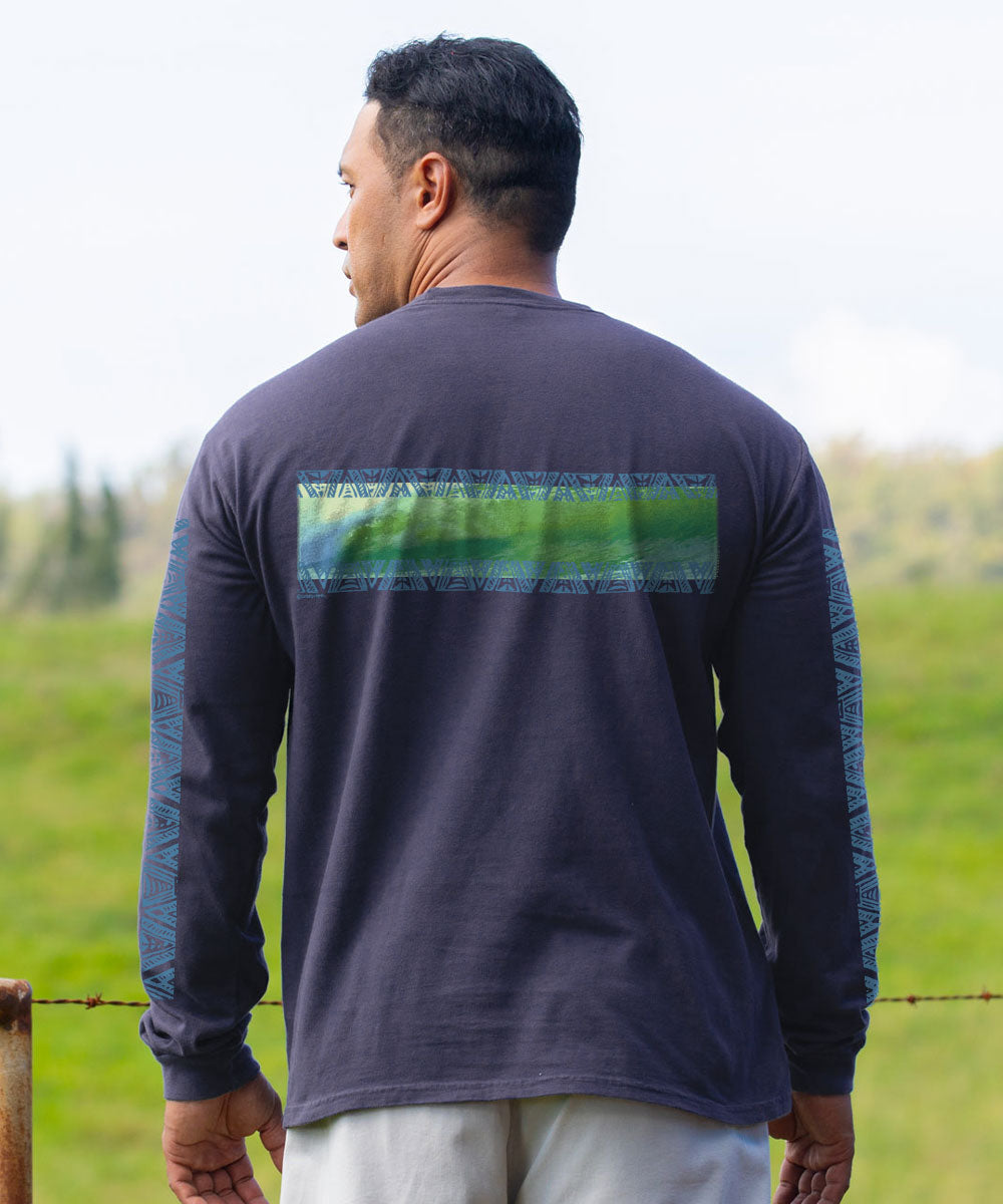 A man viewed from behind wearing a dark navy long-sleeve shirt with a green and blue textured horizontal stripe across the upper back and patterned sleeves, standing outdoors in a grassy field. View 3