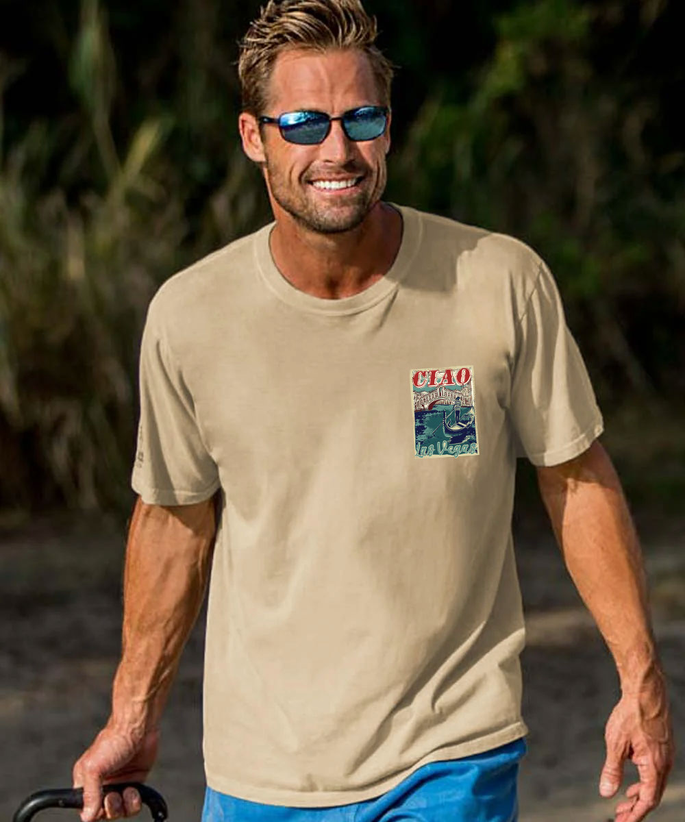 A man wearing a beige short-sleeve t-shirt with a colorful 'CIAO' graphic on the left chest, paired with blue shorts, set against a blurred outdoor background. View 3