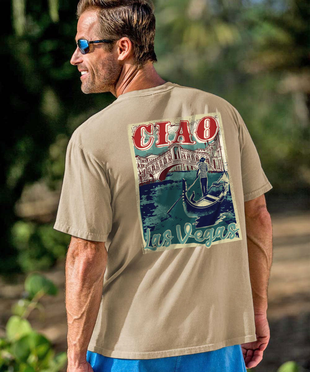 A man wearing a beige graphic t-shirt with a 'CIAO Las Vegas' print on the back, photographed outdoors against a blurred green background. View 2
