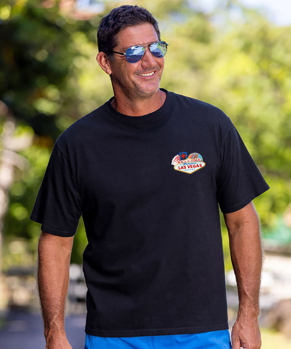 A man wearing a black short-sleeve t-shirt with a small 'Las Vegas' cartoon graphic on the left chest, set against a blurred green outdoor background. View 3