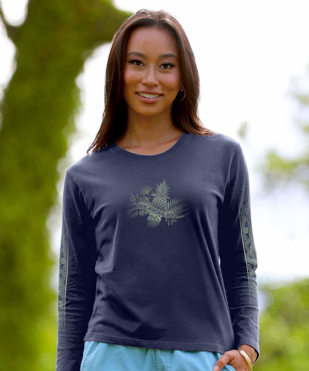 A woman wearing a dark navy long-sleeve t-shirt with a light sage green pinecone and fern graphic on the chest, set against a blurred green outdoor background. View 2