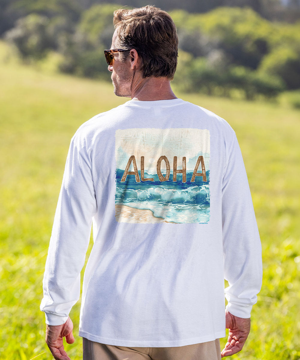 A man wearing a white long-sleeve t-shirt with a graphic print of 'ALOHA' over a beach scene, standing in a grassy field. View 2