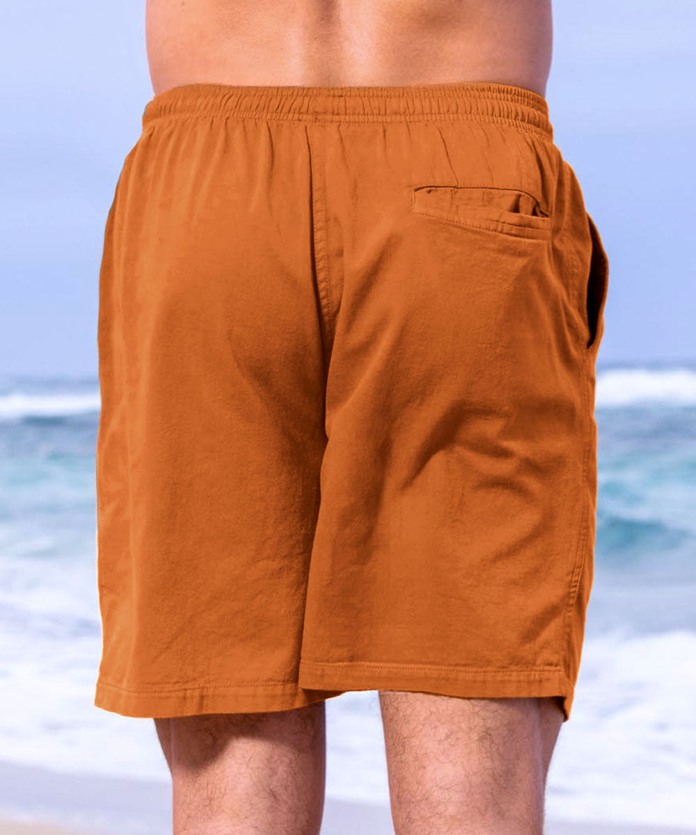 Mustard yellow shorts worn by a person with a blurred ocean background View 3