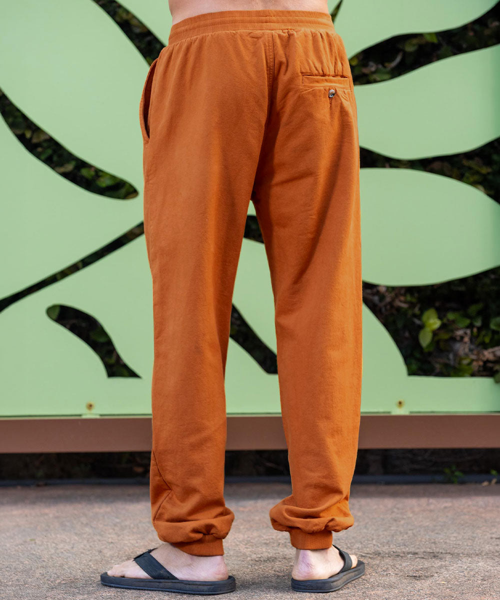 Person wearing mustard yellow pants standing against a green wall with black abstract designs. View 3