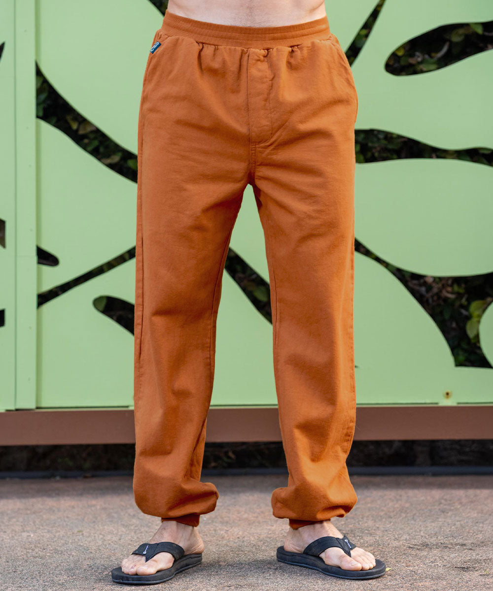 Person wearing mustard yellow pants standing against a green wall with black abstract designs. View 2