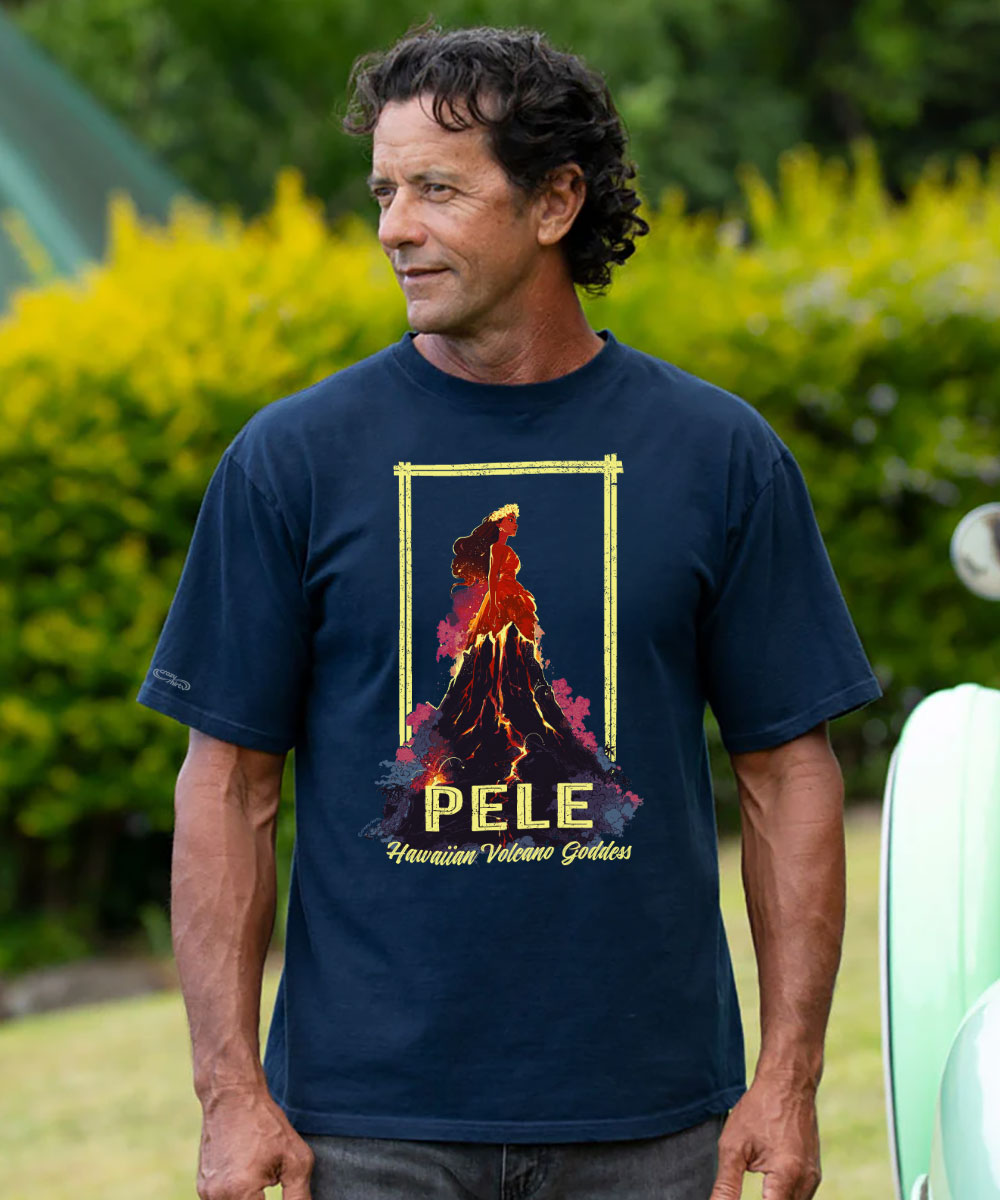 A man wearing a navy blue graphic t-shirt featuring a lava volcano design with the text 'PELE' and 'Hawaiian Volcano God', set against a blurred green garden background. View 2