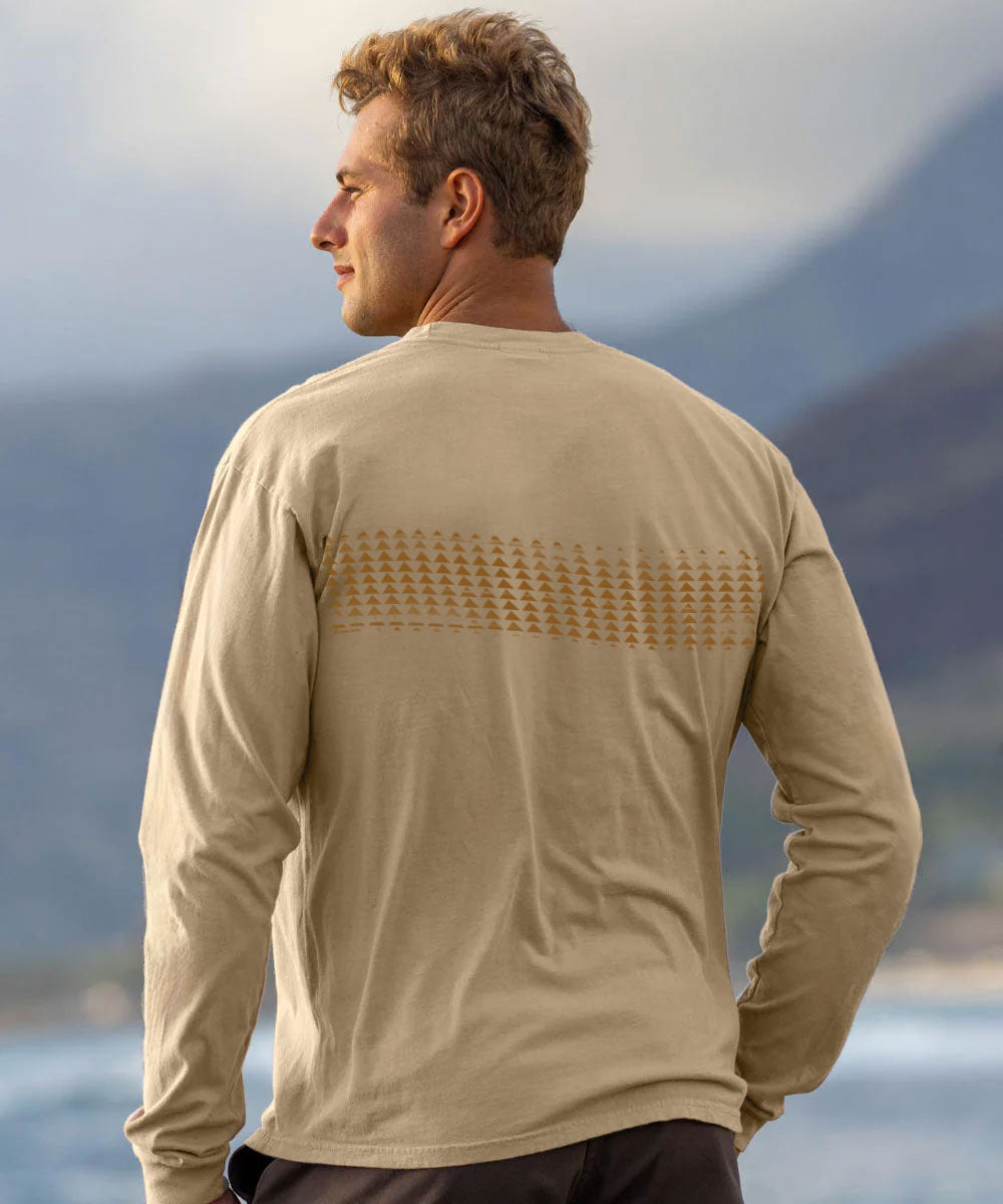 A man wearing a beige long-sleeve shirt, viewed from behind, standing outdoors with a blurred mountain and water background. View 3