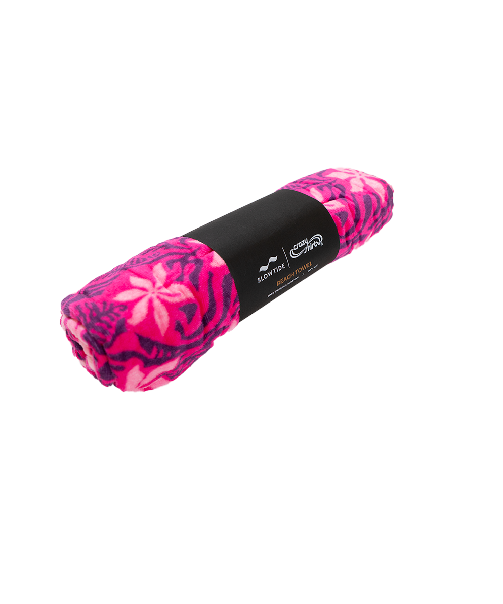 A rolled-up fleece blanket featuring a vibrant pink and purple abstract pattern, wrapped in a black paper band with white branding. View 2