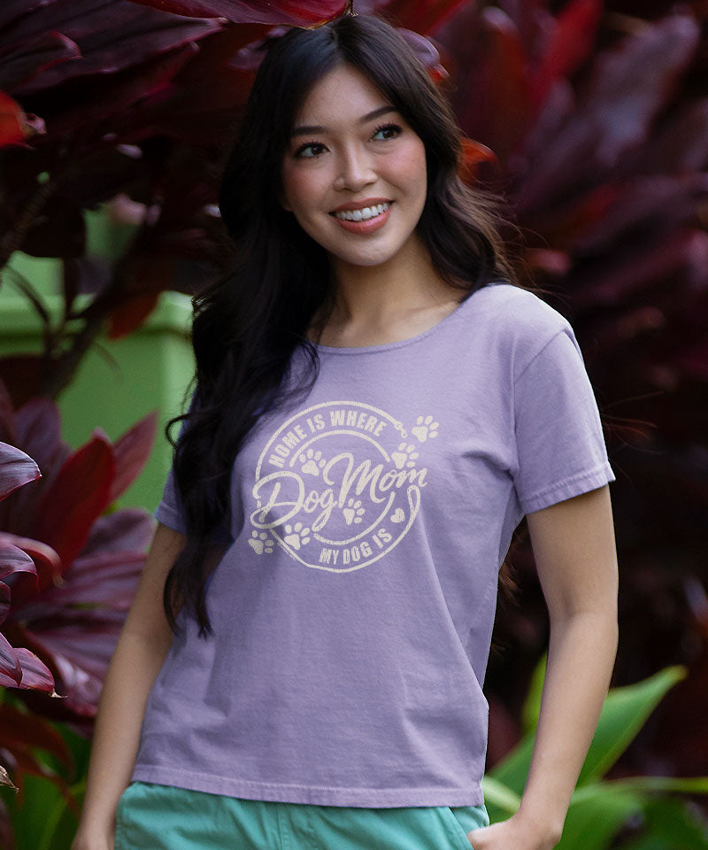 Woman wearing a purple t-shirt with 'Home is where my dog mom is' design, standing in front of tropical plants. View 2