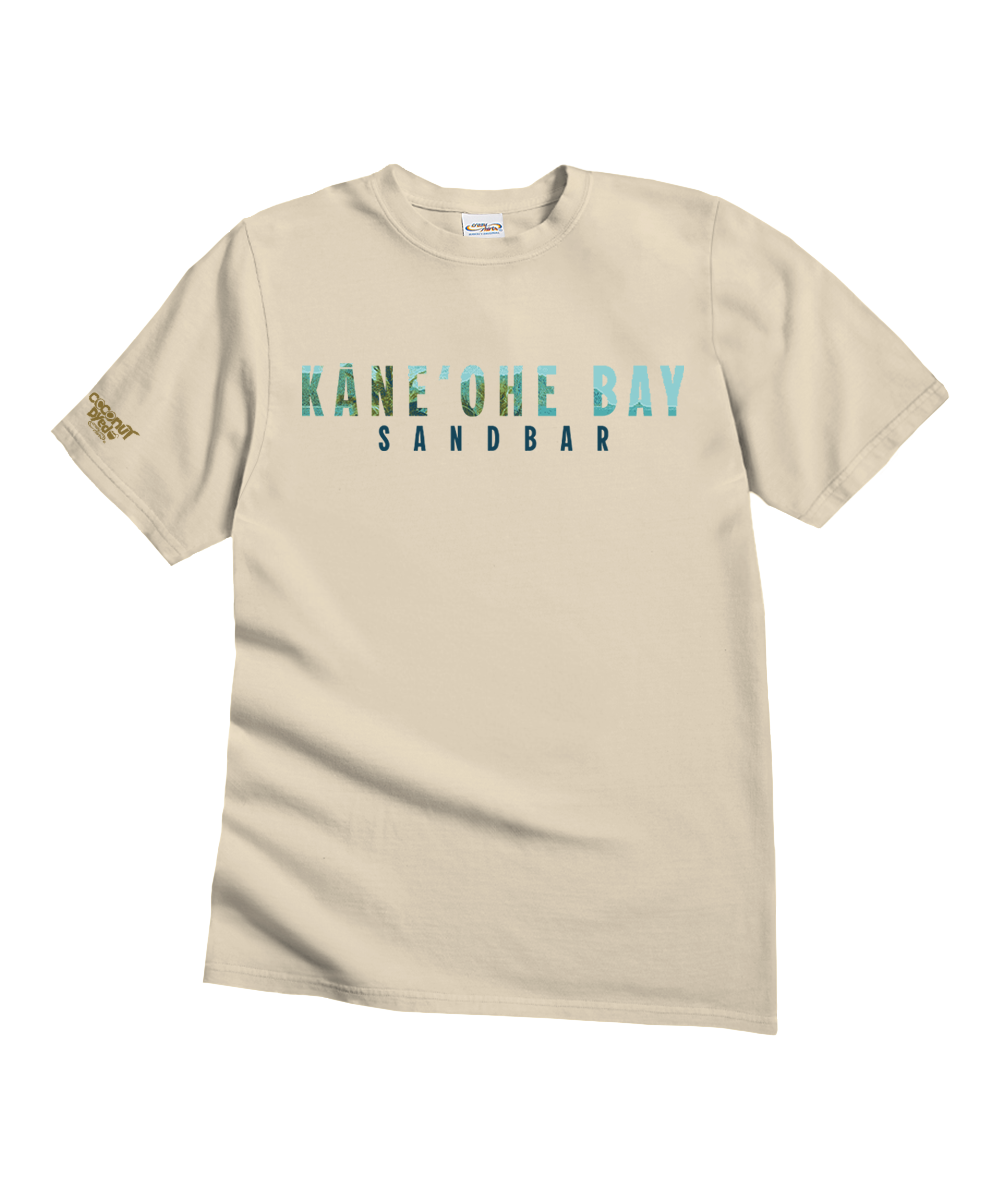 A beige short-sleeve t-shirt with 'KANE'OHE BAY' and 'SANDBAR' printed on the chest in a teal-to-blue gradient, with a small gold logo on the left sleeve, shown on a plain white background. View 4