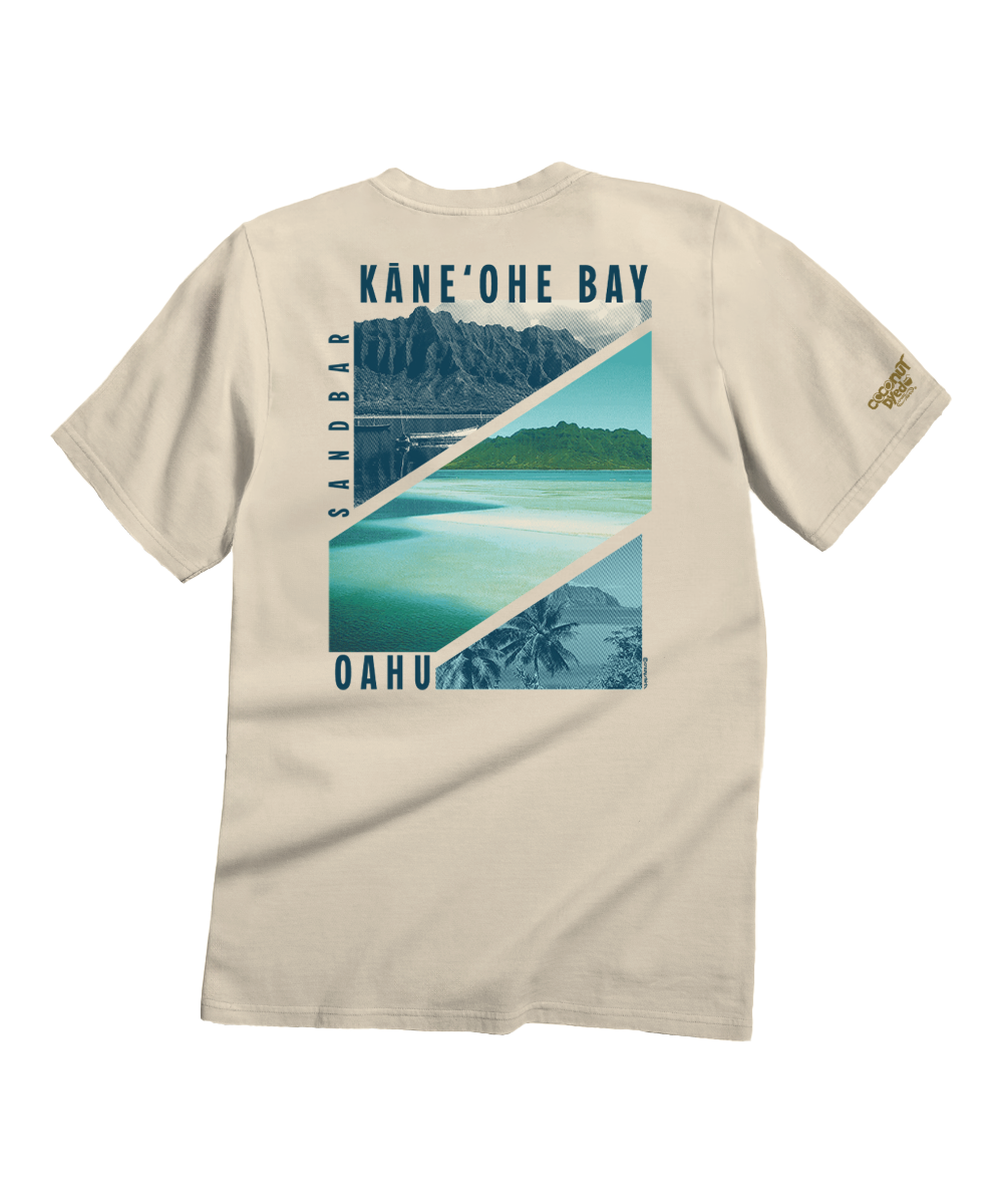 A beige crewneck t-shirt shown from the back, featuring a large graphic print of Kamehōhe Bay in Oahu with a mountain, beach, and palm trees in shades of blue and green, and 'KANE'OHE BAY' and 'OAHU' printed in blue text. View 1