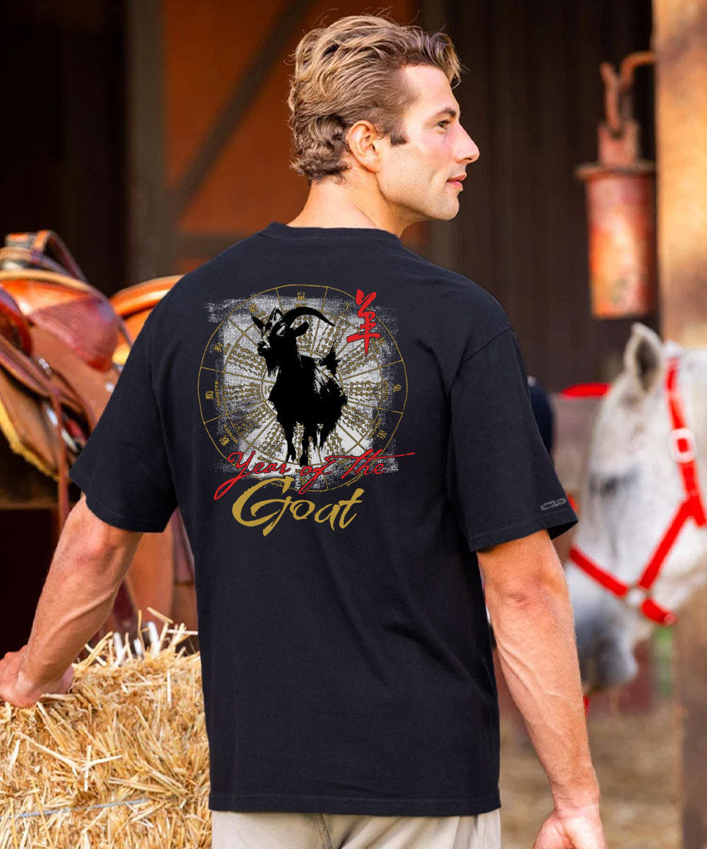 A man wearing a black short-sleeve crewneck t-shirt, shown from the back in a rustic barn setting with hay and a horse in the background. View 2