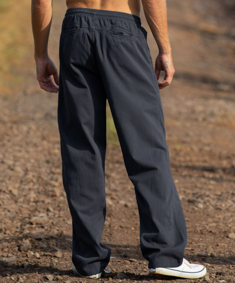 A person shown from the back wearing dark charcoal gray wide-leg pants, standing outdoors on a gravel path. View 3