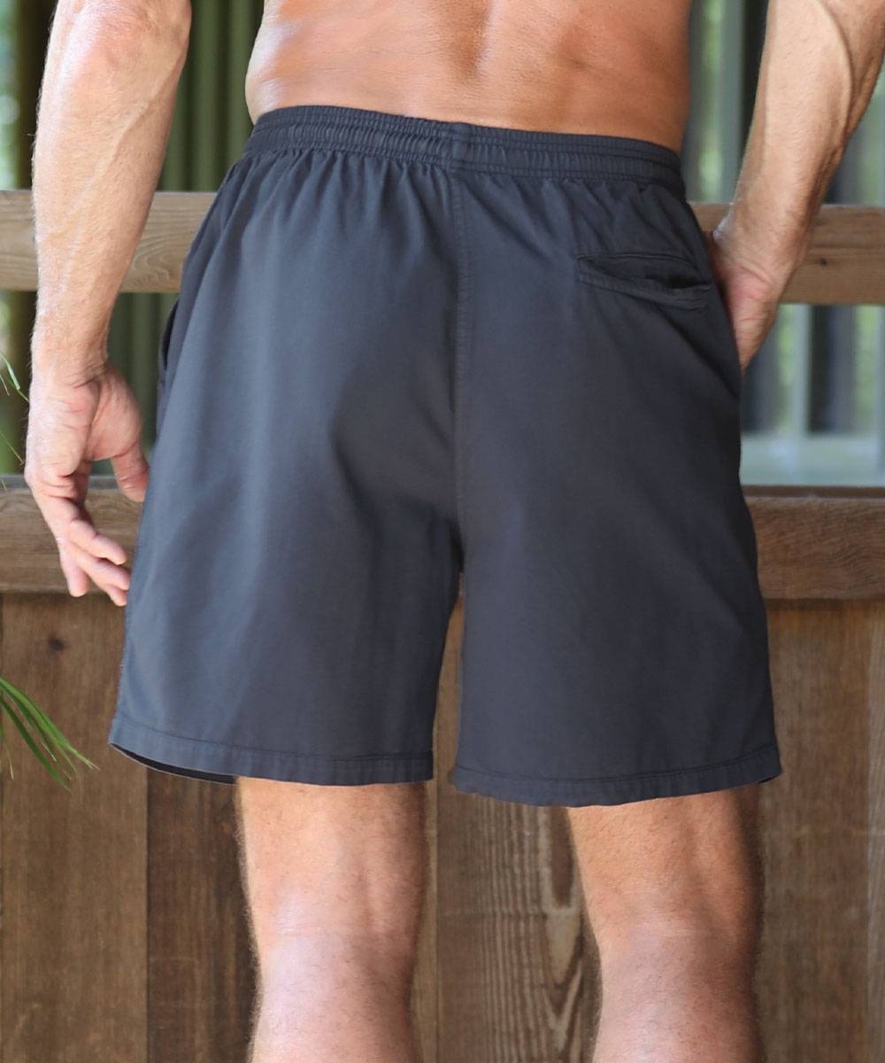 A man wearing dark gray athletic shorts, shown from the back, standing outdoors against a wooden fence. View 3