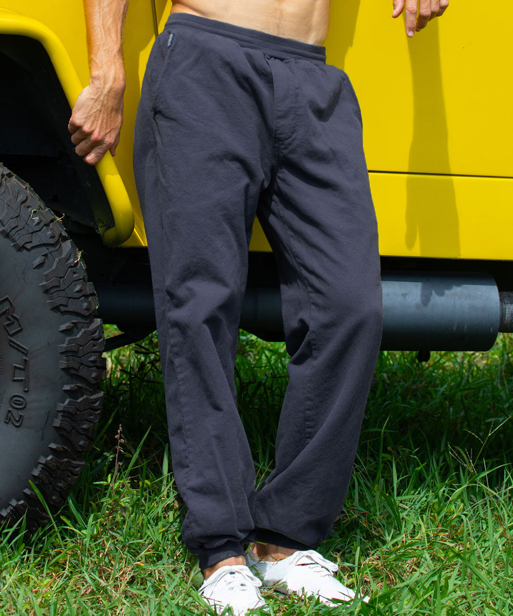 A person standing outdoors on grass beside a bright yellow vehicle, wearing dark charcoal gray jogger-style pants with a back pocket and white sneakers. View 2