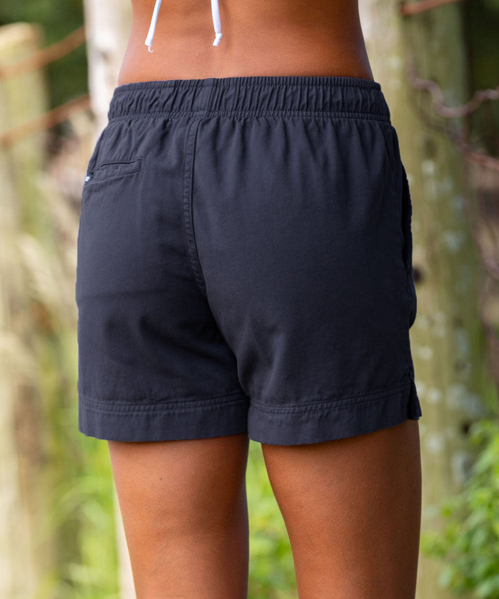 Rear view of a person wearing dark navy drawstring shorts outdoors, with a blurred natural background of trees and foliage. View 3