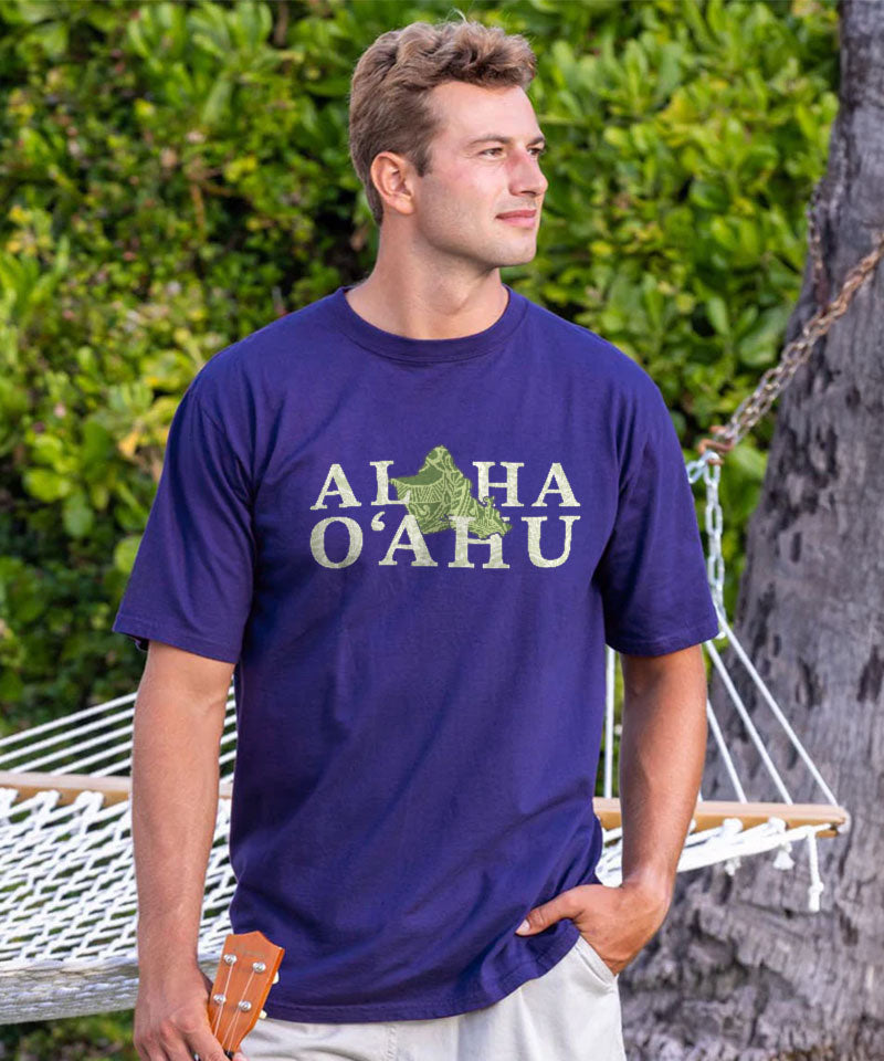 Man wearing a blue t-shirt with 'ALOHA O'AHU' text, standing outdoors near a hammock. View 2