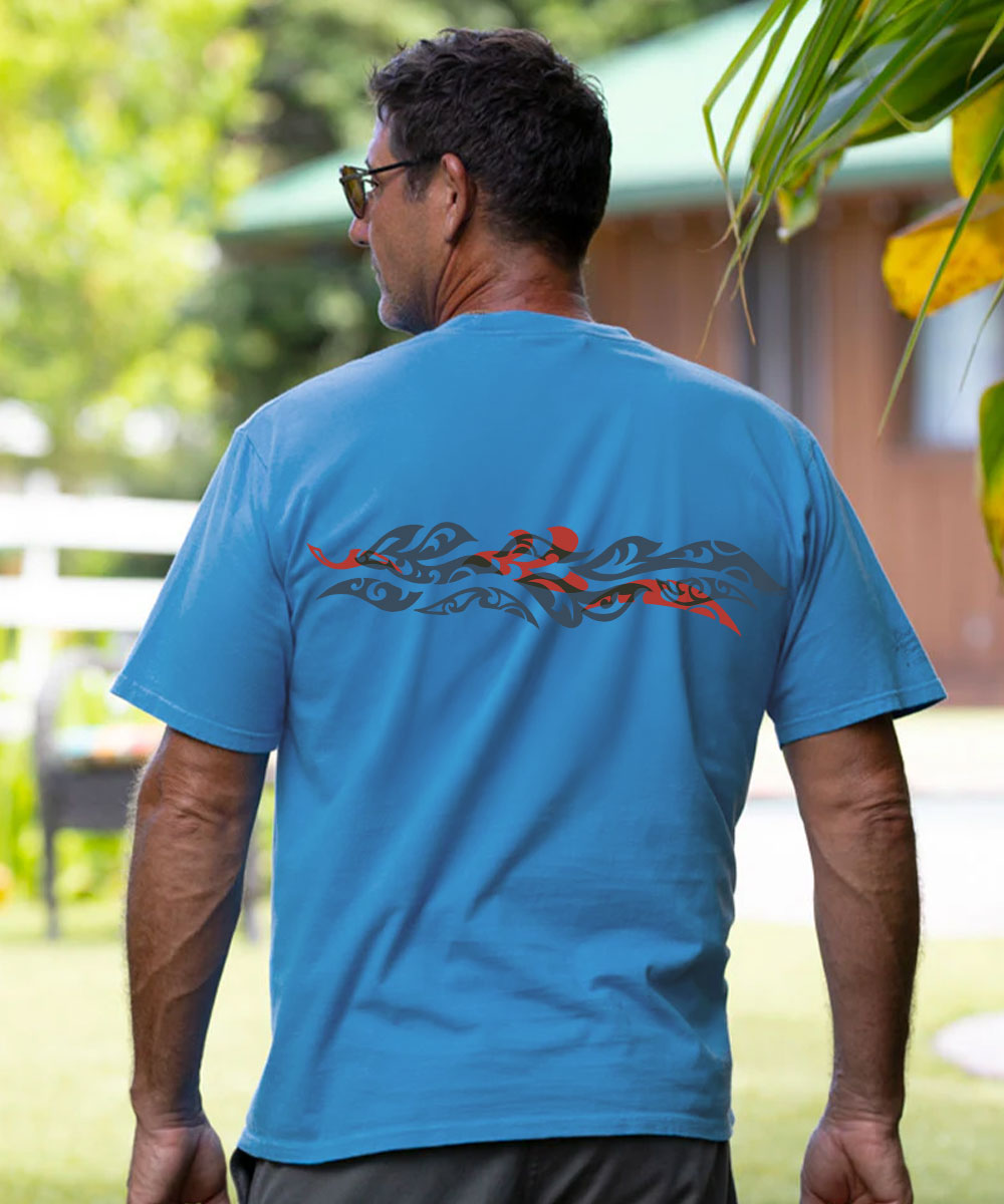A man viewed from behind wearing a bright blue short-sleeve t-shirt with a red and black tribal-style graphic across the upper back, set against a blurred outdoor background. View 3