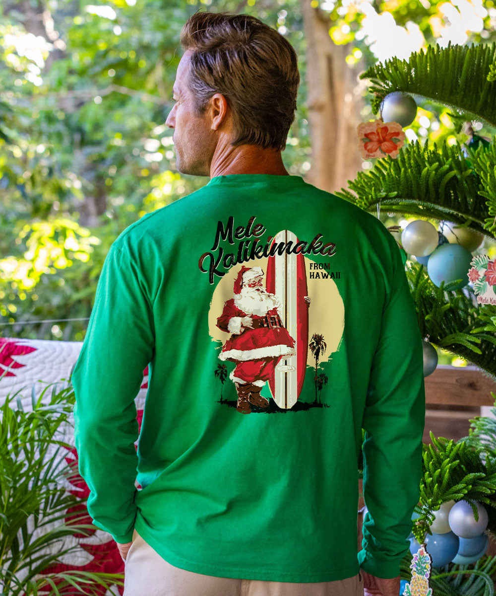A man wearing a bright green long-sleeve t-shirt with a  blurred background of green plants and holiday decorations. Wearing a christmas shirt